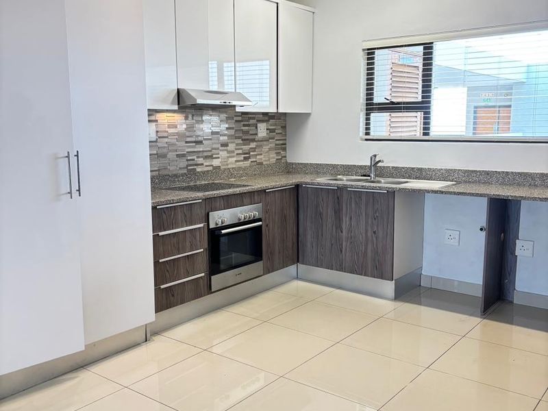 Modern kitchen featuring high-gloss white upper cabinetry, wood-grain lower cabinets, granite countertops, tiled backsplash, and built-in oven with extractor fan.