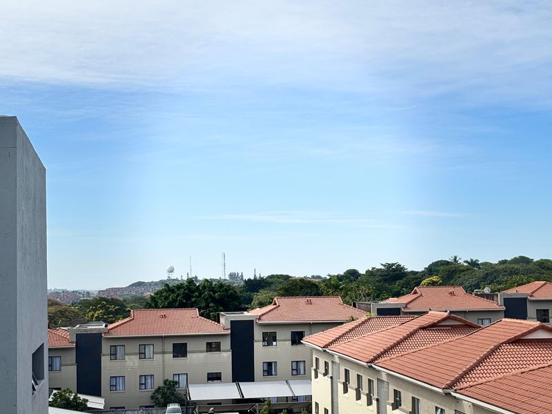 Elevated view overlooking the apartment complex grounds, featuring tiled roofs, paved parking areas, and surrounding greenery.