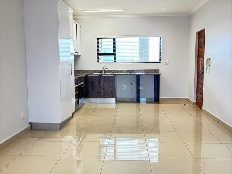 A modern open-plan kitchen featuring high-gloss cabinetry, granite countertops, integrated oven, and polished porcelain floor tiles in a bright, neutral space.