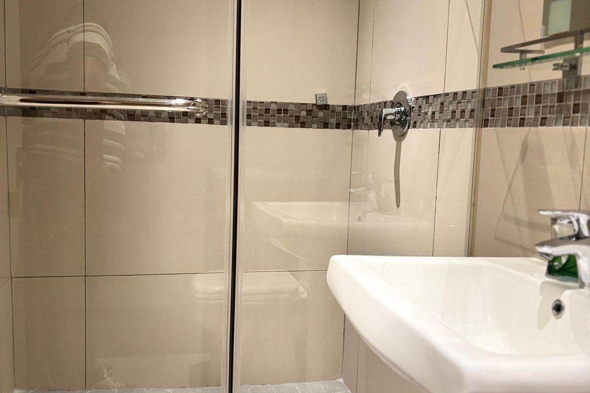A compact bathroom featuring a glass-enclosed shower with mosaic tile accents and a white pedestal sink.