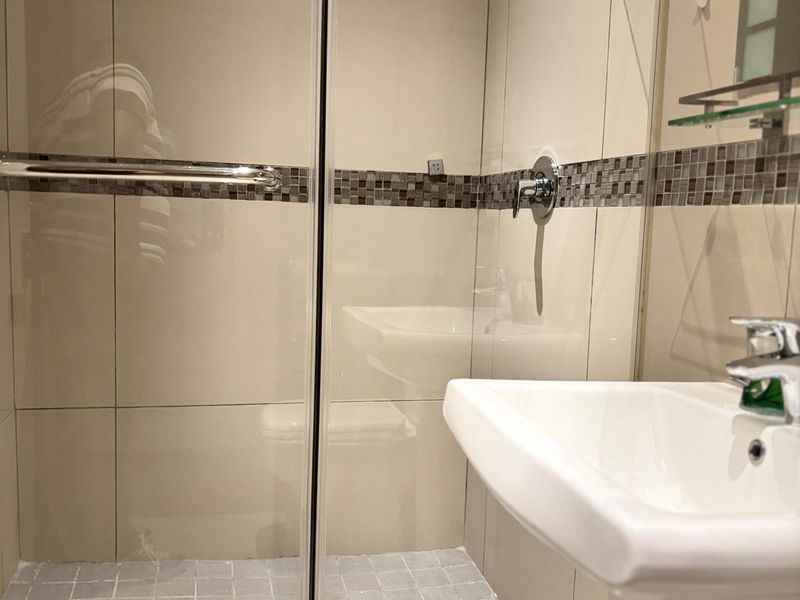 A compact bathroom featuring a glass-enclosed shower with mosaic tile accents and a white pedestal sink.