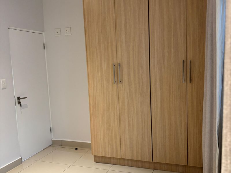 A clean bedroom featuring light-toned tiled flooring and built-in wooden cabinetry with modern handles.