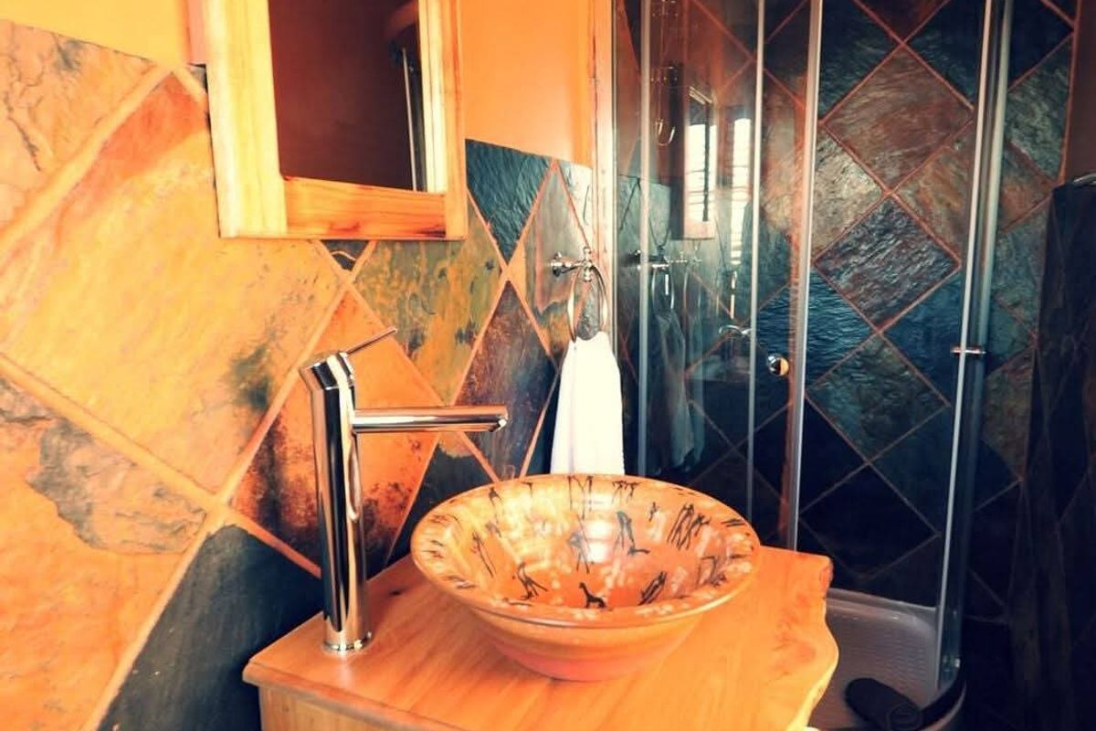 A compact bathroom featuring a corner shower enclosure, a custom wooden vanity with a vessel sink, and decorative slate-style wall tiling.