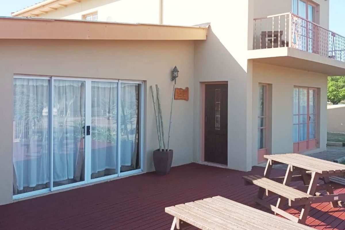 Rear view of the property featuring a large wooden deck, sliding glass doors, and an upper-level balcony with metal railings.