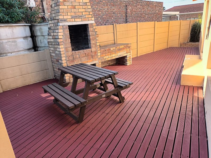 Outdoor patio area featuring a built-in brick fireplace and barbecue station, complemented by durable composite decking and enclosed by perimeter boundary walls.