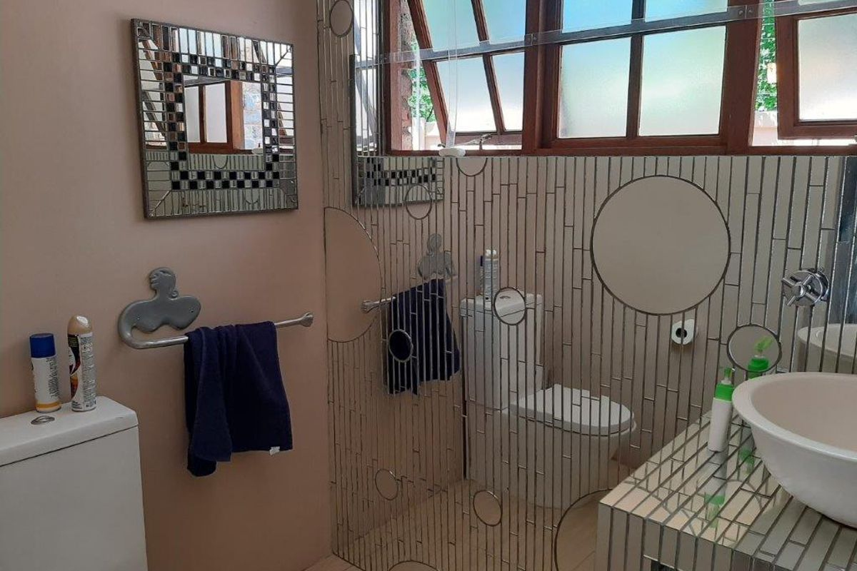 A bathroom featuring a vessel sink, vanity, and toilet, with decorative tiled wall accents and natural light from the window.