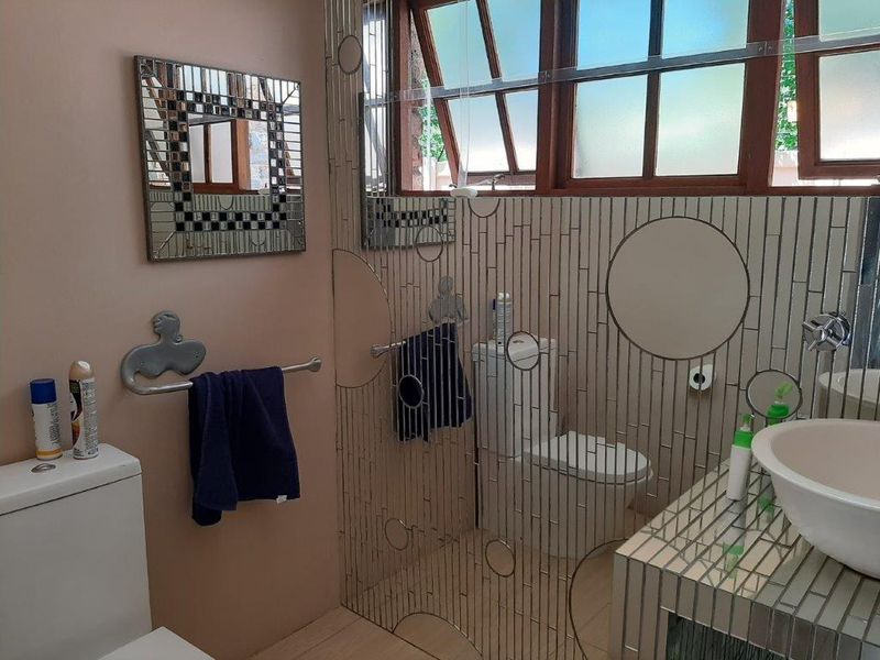 A bathroom featuring a vessel sink, vanity, and toilet, with decorative tiled wall accents and natural light from the window.