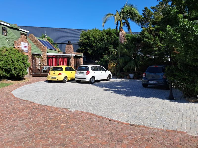 Front exterior view of the property featuring a paved driveway, brick facade, solar panels, and a small timber deck area.
