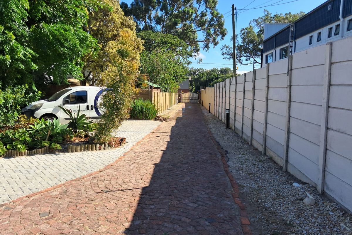 A paved driveway leading towards the property entrance, featuring a precast concrete boundary wall and established garden landscaping.