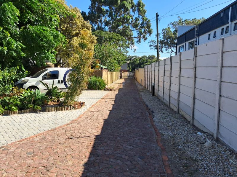 A paved driveway leading towards the property entrance, featuring a precast concrete boundary wall and established garden landscaping.