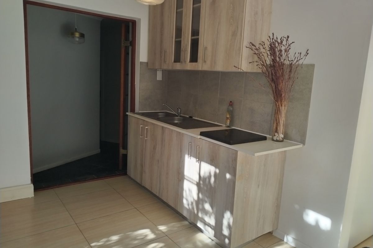 A compact kitchen featuring light wood-finish cabinetry, a tiled backsplash, a stainless steel sink, and a built-in ceramic hob.