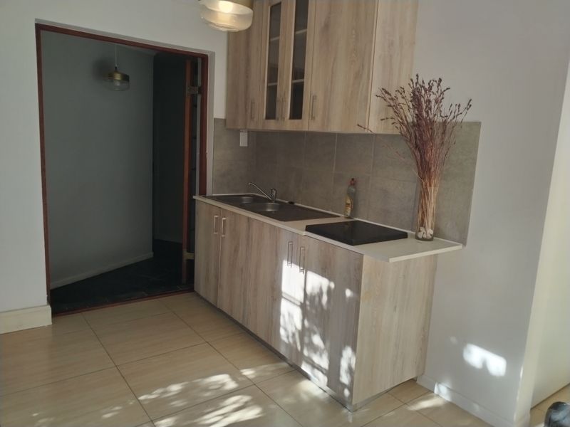 A compact kitchen featuring light wood-finish cabinetry, a tiled backsplash, a stainless steel sink, and a built-in ceramic hob.