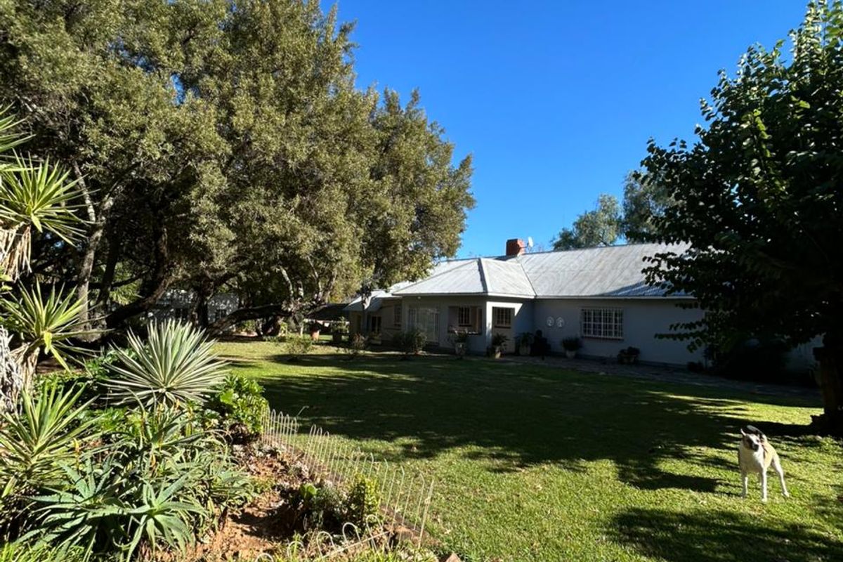 A view of the rear garden and lawn area leading to the farmhouse exterior, featuring mature trees and established landscaping.