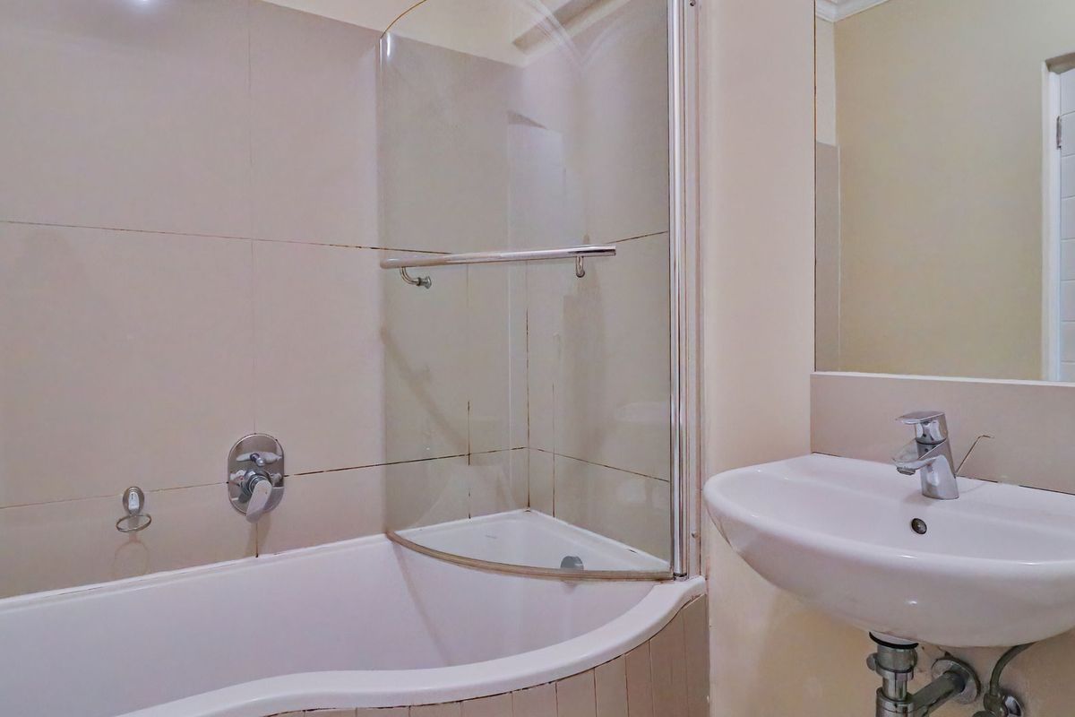 A functional bathroom featuring a bathtub with a glass shower screen, wall-mounted mixer tap, and a pedestal basin with a mirror.