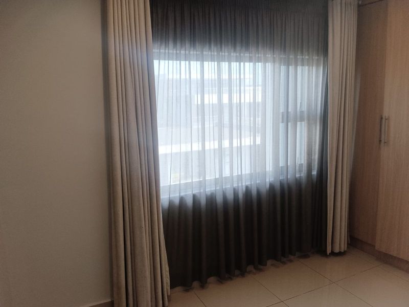 A bedroom featuring tiled flooring, built-in wooden cabinetry, and large windows dressed with floor-to-ceiling curtains.