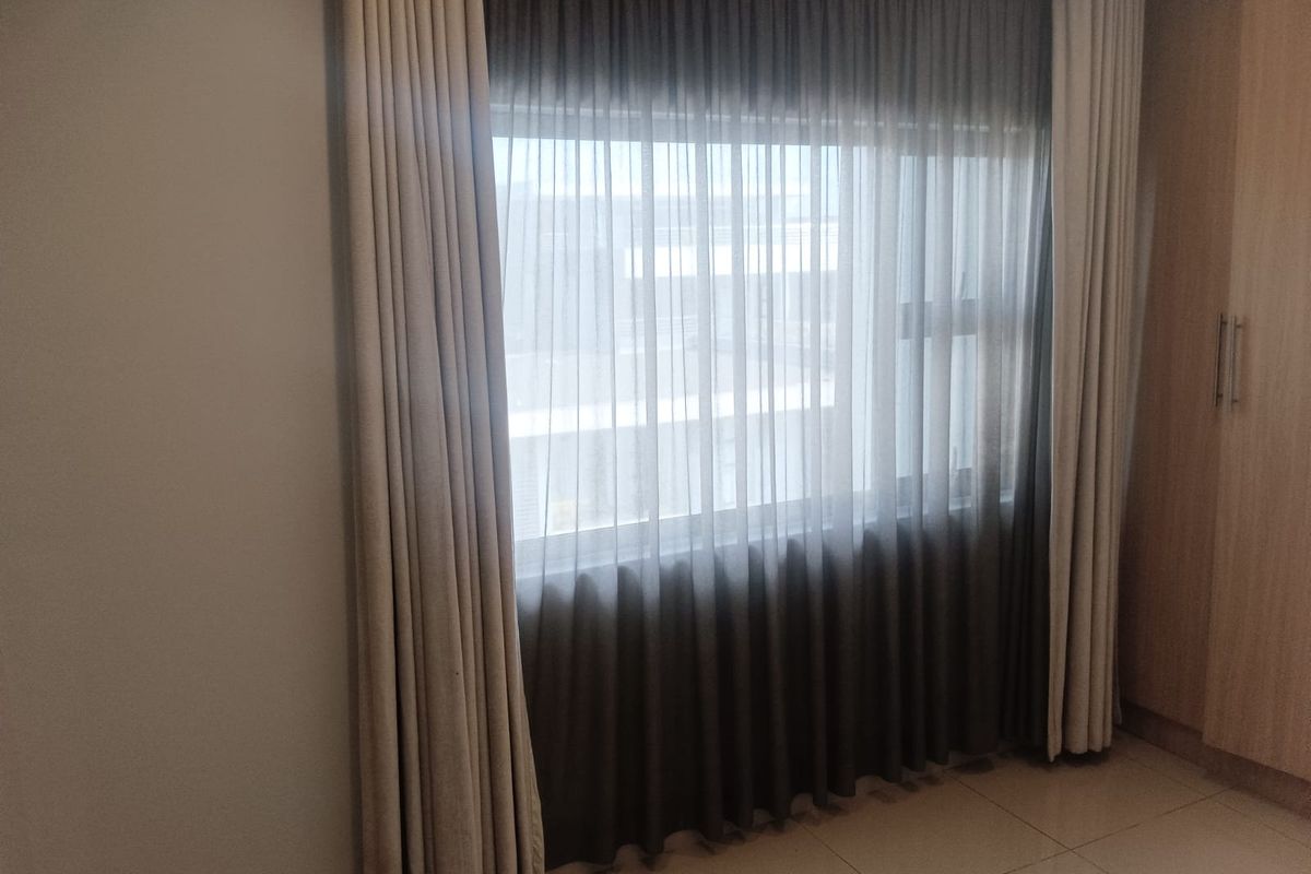 A bedroom featuring tiled flooring, built-in wooden cabinetry, and large windows dressed with floor-to-ceiling curtains.