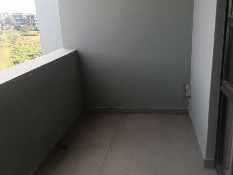 A compact, covered balcony featuring tiled flooring and neutral wall finishes, offering an open view of the surrounding area.