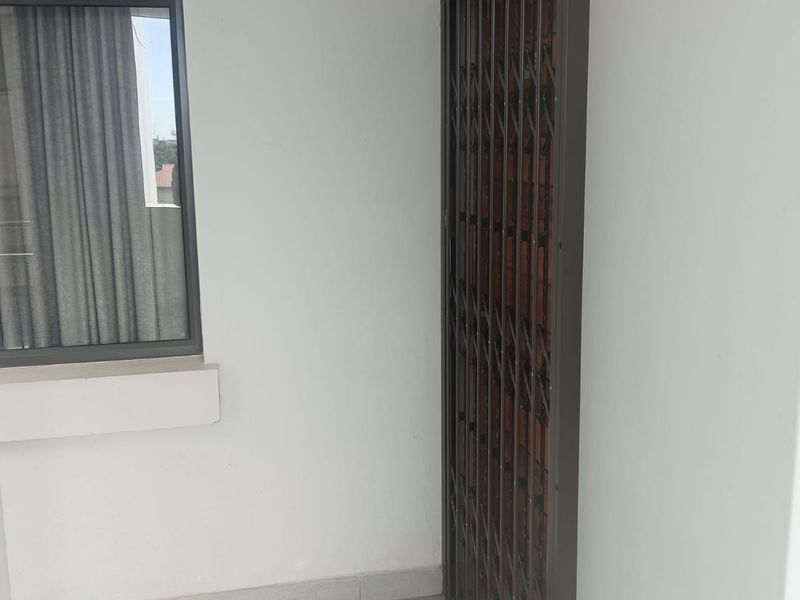 A functional entryway or transition space featuring tiled flooring, a secure metal security gate, and a window with fitted blinds.