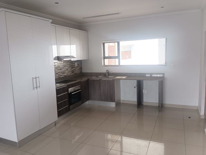 Modern kitchen featuring sleek white and wood-grain cabinetry, granite countertops, built-in oven, hob, extractor fan, and tiled flooring.