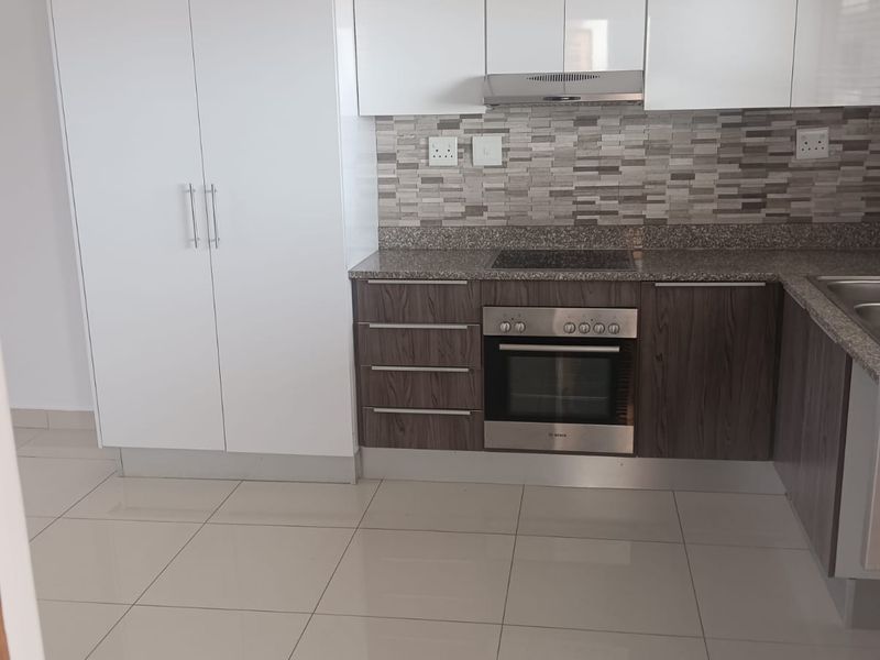 Modern kitchen featuring white upper cabinetry, wood-grain lower cabinets, granite countertops, tiled backsplash, and built-in oven with extractor fan.