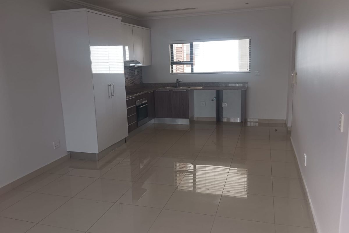 A clean, modern kitchen featuring tiled flooring, built-in cabinetry, a stainless steel sink, and an integrated oven with an extractor fan.