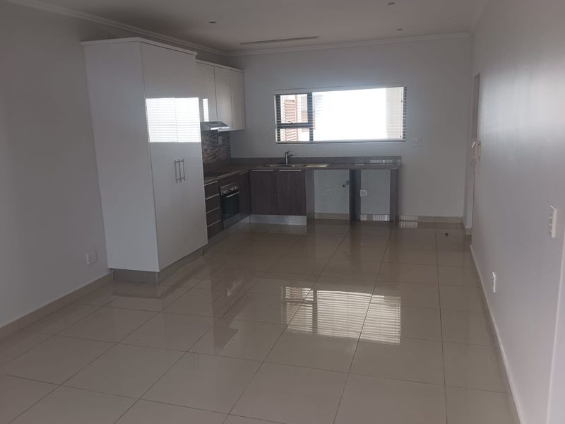 A clean, modern kitchen featuring tiled flooring, built-in cabinetry, a stainless steel sink, and an integrated oven with an extractor fan.