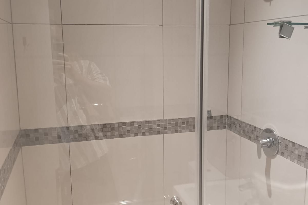 A modern shower enclosure featuring neutral wall tiles with a decorative mosaic border, glass door, and chrome shower fixtures.