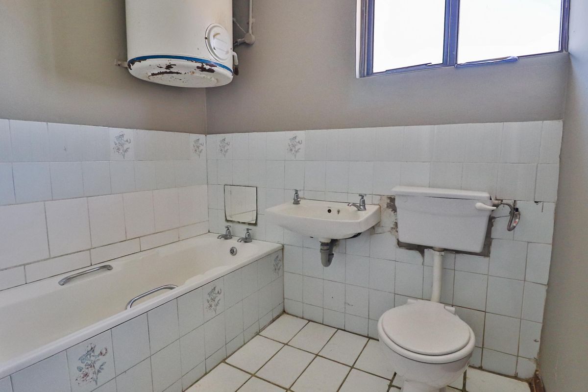 A dated bathroom featuring a standard bathtub, wall-mounted basin, and toilet, with visible wear to the wall tiles and water heater unit.