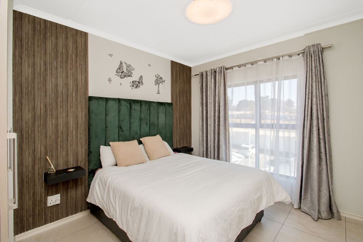 A well-maintained bedroom featuring wood-look wall paneling, tiled flooring, and a large window with curtain tracks.