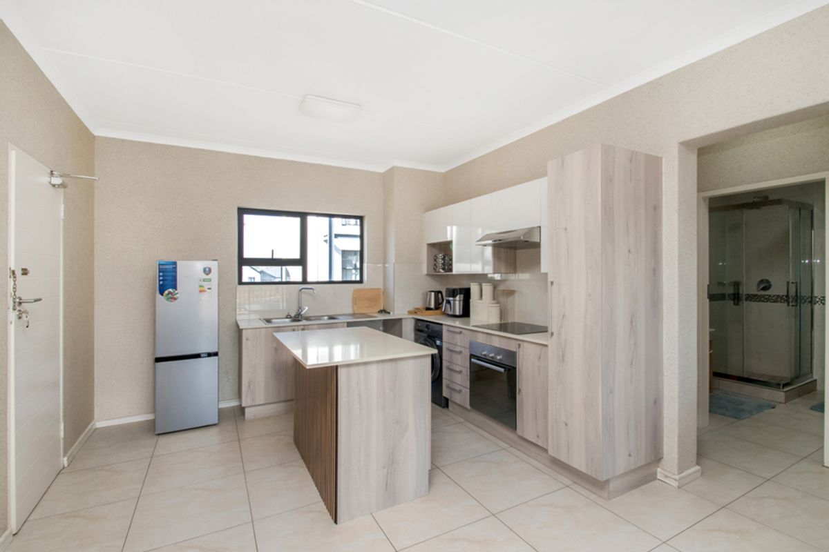 Modern kitchen featuring light wood-grain cabinetry, stone countertops, a central island, built-in oven, hob, and extractor fan, with tiled flooring throughout.