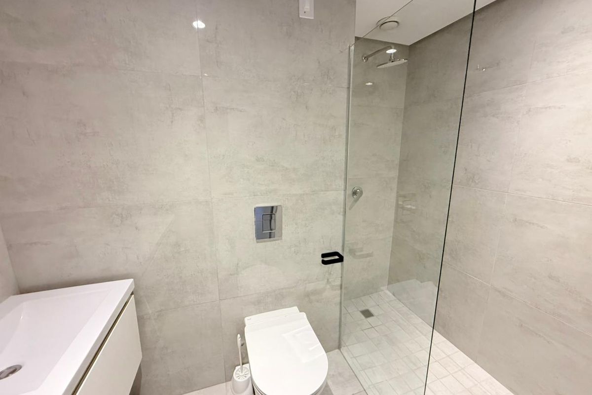 Modern bathroom featuring large-format grey wall tiles, a wall-mounted toilet with concealed cistern, and a walk-in shower with a glass partition.