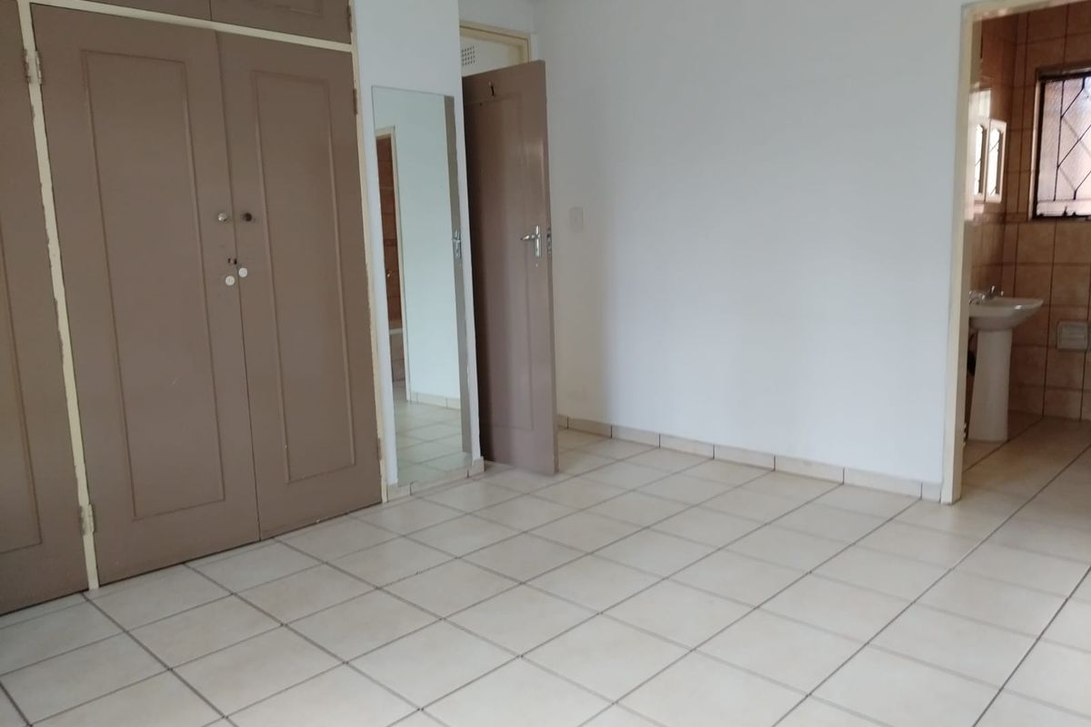 A spacious bedroom featuring built-in cupboards, tiled flooring, and an en-suite bathroom entrance.