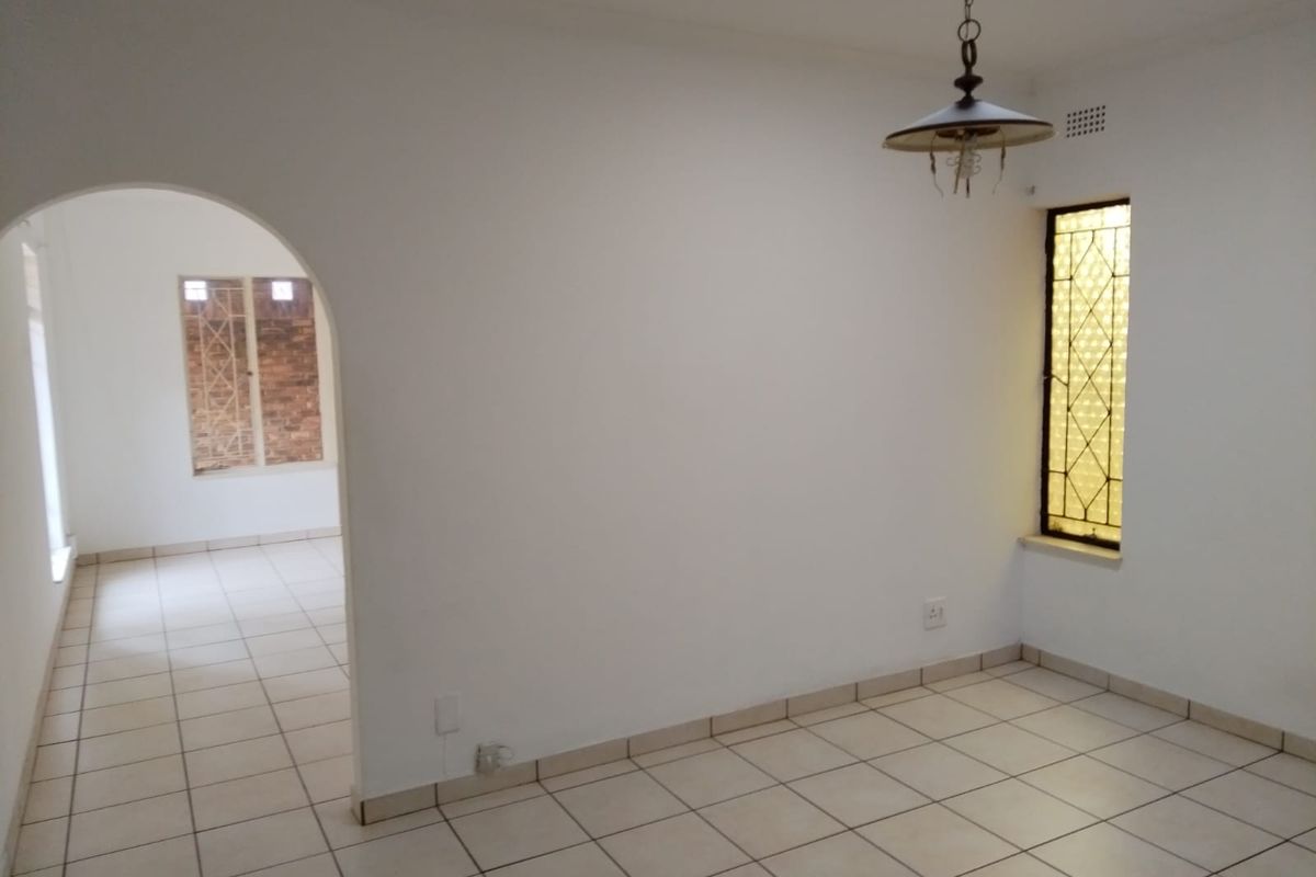 An empty living area featuring tiled flooring, an arched doorway leading to an adjacent room, and decorative leaded glass windows.
