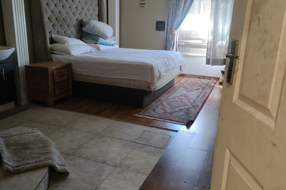 A bedroom featuring a mix of tiled and wood-look flooring, including an integrated vanity area with a basin and built-in headboard structure.