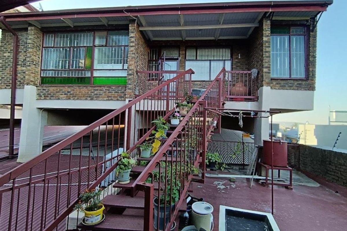 Exterior view of an apartment building featuring a raised balcony, brick facade, and an external metal staircase leading to the upper level entrance.