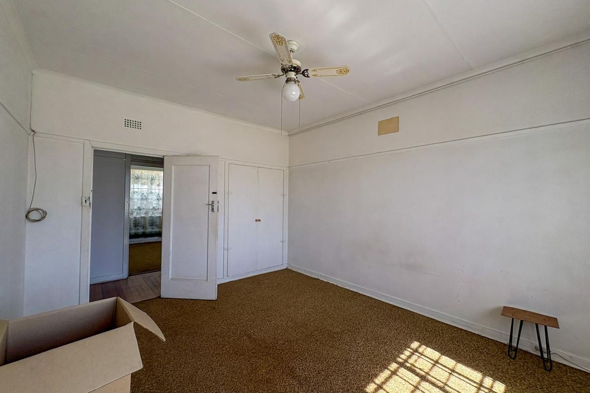 An empty bedroom featuring built-in cupboards, a ceiling fan, and a picture rail, requiring cosmetic updates to the flooring and wall finishes.