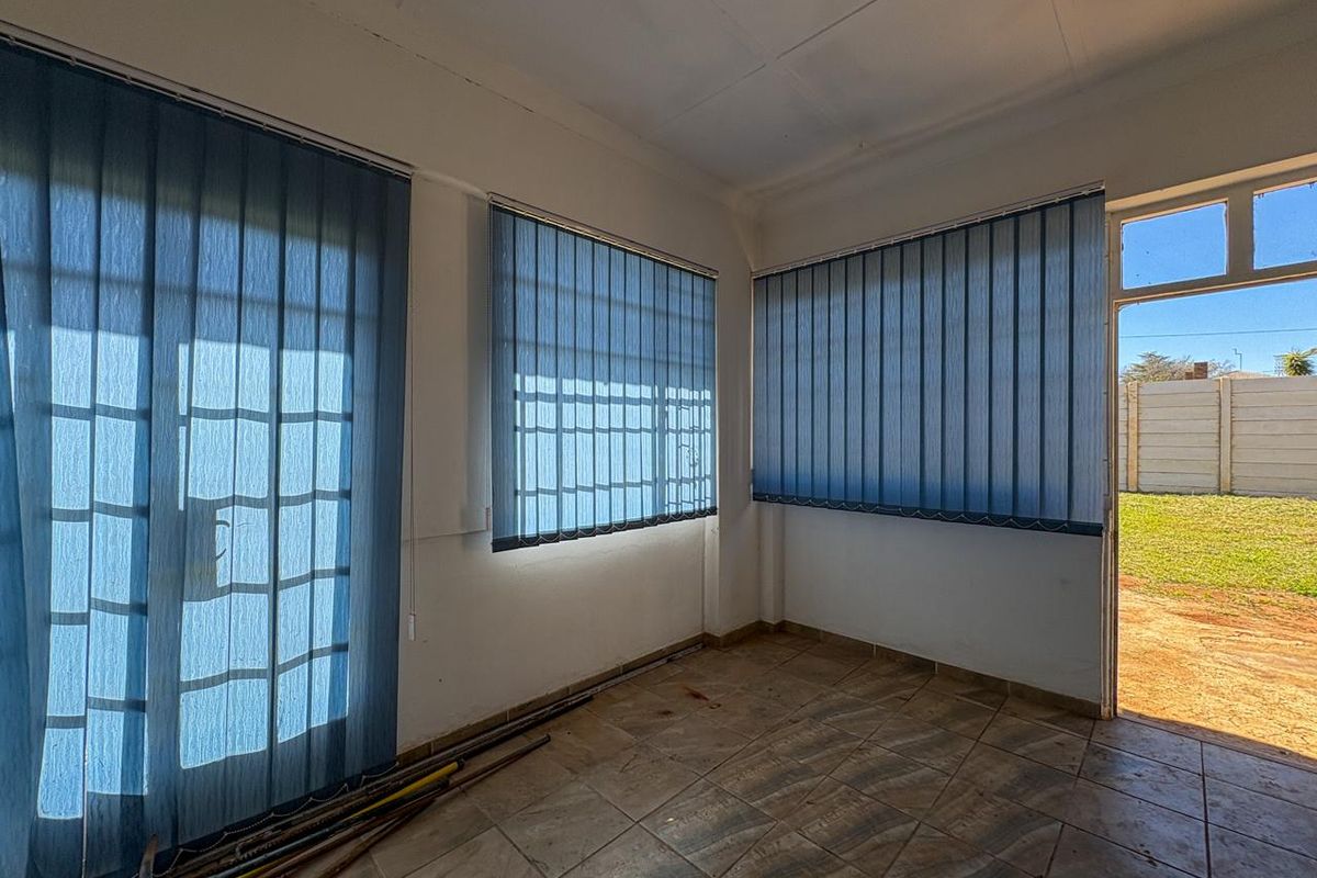 An empty living area featuring tiled flooring, vertical blinds, and direct access to the rear garden through a glass panel door.