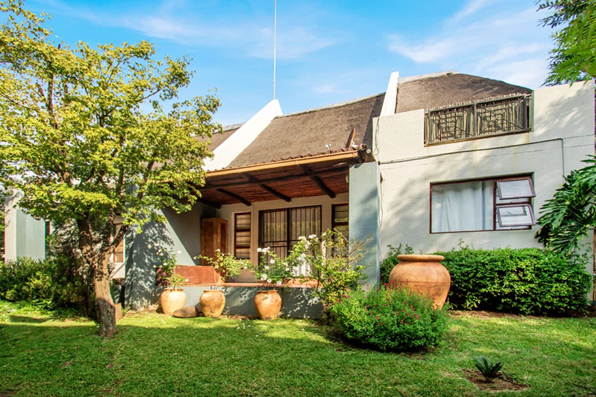 Rear view of a townhouse featuring a thatched roof, a covered patio area, and an upper-level balcony overlooking a private garden.