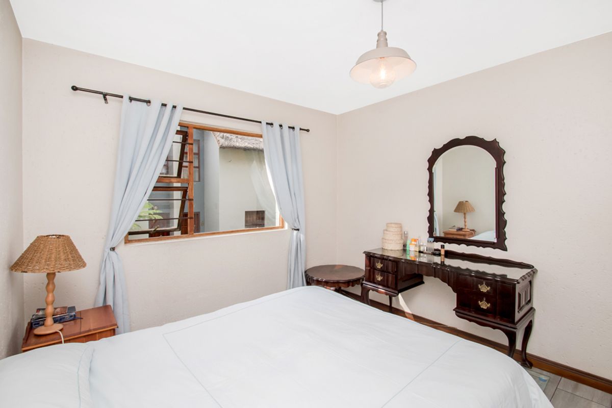 A well-lit bedroom featuring neutral walls, timber window frames, and a classic pendant light fixture, offering a comfortable and functional living space.