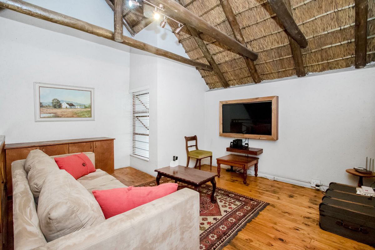 Living room featuring a high vaulted thatched ceiling with exposed timber rafters, timber flooring, and natural light through venetian blinds.