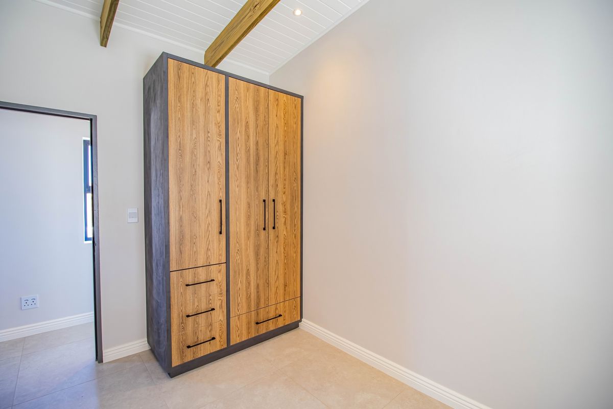 A bedroom featuring a modern, built-in wooden wardrobe with integrated drawers and dark trim, set against a neutral interior with exposed ceiling beams.