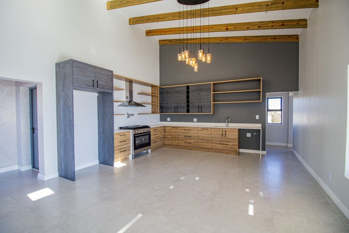 Modern open-plan kitchen featuring timber cabinetry, stone countertops, stainless steel gas stove, extractor fan, and exposed wooden ceiling beams.