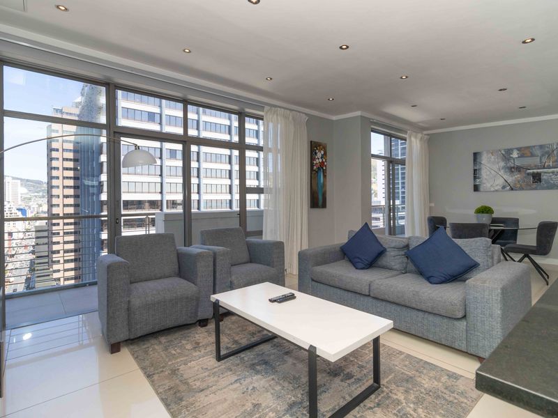 Bright open-plan living and dining area featuring large floor-to-ceiling windows, recessed downlighting, and modern tiled flooring with access to a balcony.