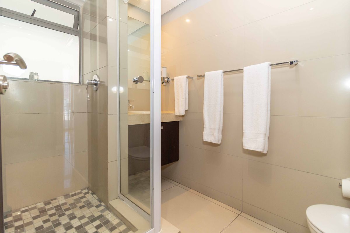 A modern bathroom featuring a glass-enclosed shower, wall-mounted vanity, and neutral ceramic tiling throughout.