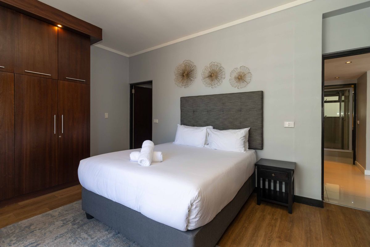 A well-maintained bedroom featuring laminate flooring, a large built-in wooden wardrobe, and neutral wall finishes with access to an adjoining bathroom.