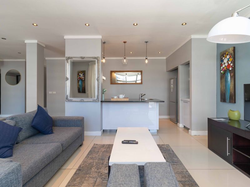 Modern open-plan living area featuring a sleek kitchen island with stone countertop, recessed lighting, and neutral tiled flooring throughout.