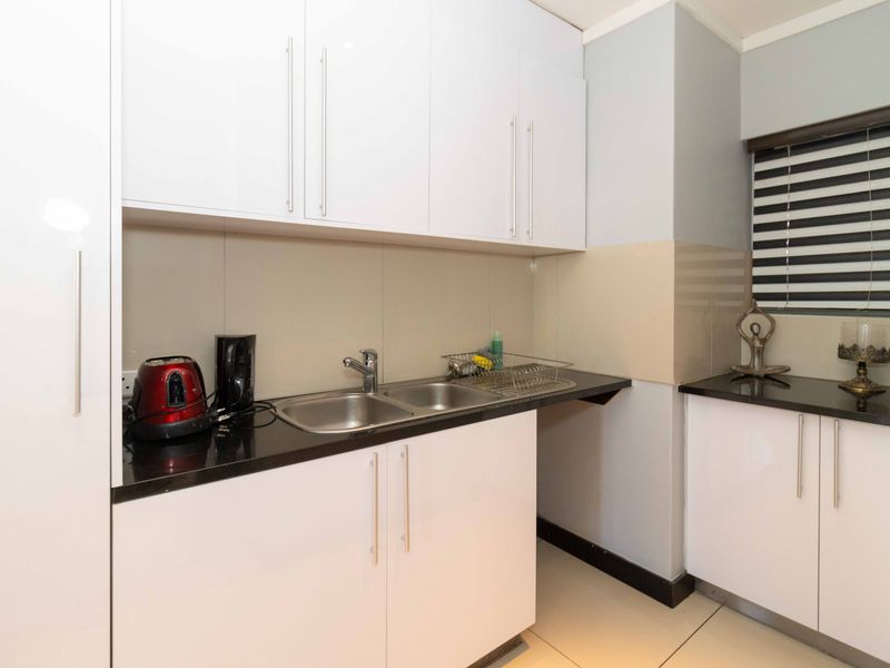 A clean and modern kitchen area featuring white cabinetry, dark granite countertops, a double bowl sink, and neutral tiled flooring.