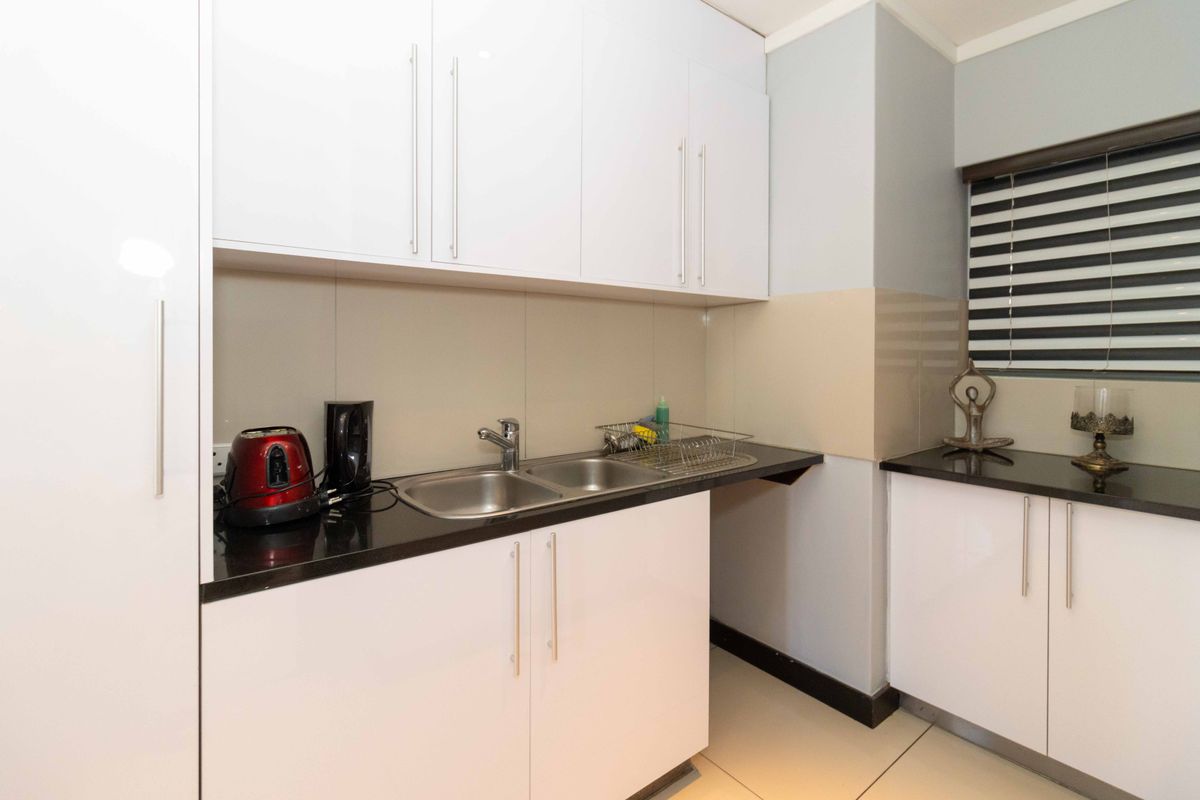 A clean and modern kitchen area featuring white cabinetry, dark granite countertops, a double bowl sink, and neutral tiled flooring.