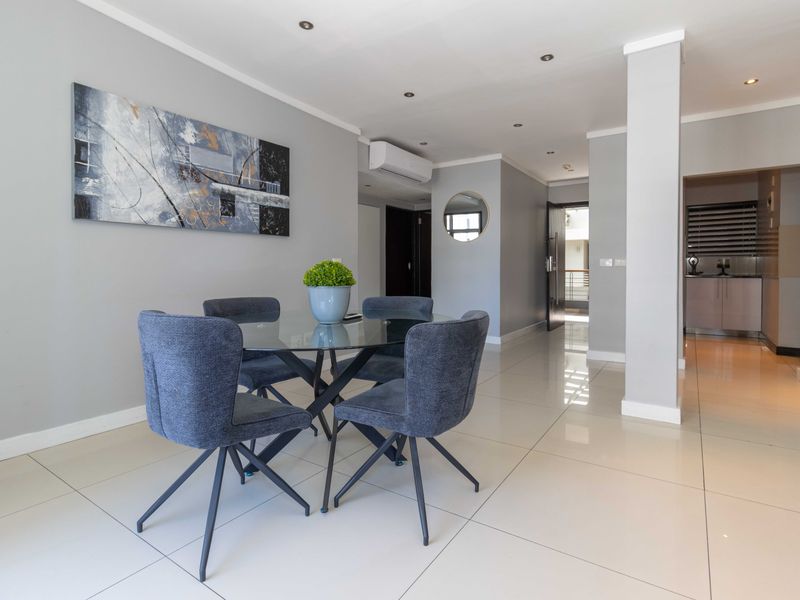Modern open-plan dining area featuring sleek porcelain floor tiles, recessed downlighting, and a wall-mounted air conditioning unit, leading into a functional kitchen space.