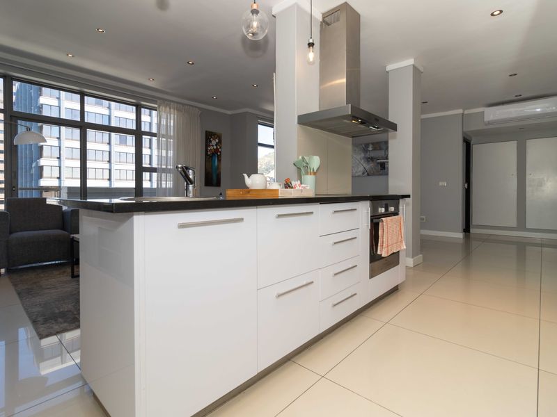 Modern open-plan kitchen and living area featuring a central island, sleek cabinetry, stainless steel appliances, and large glass doors leading to a balcony.